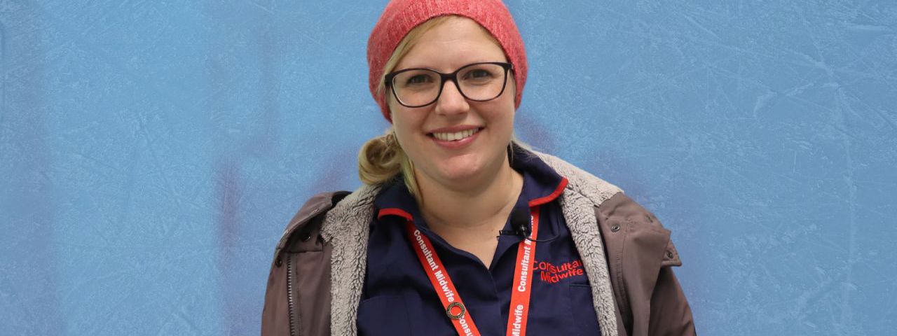 A pregnant consultant midwife smiling whilst wearing winter coat and a hat